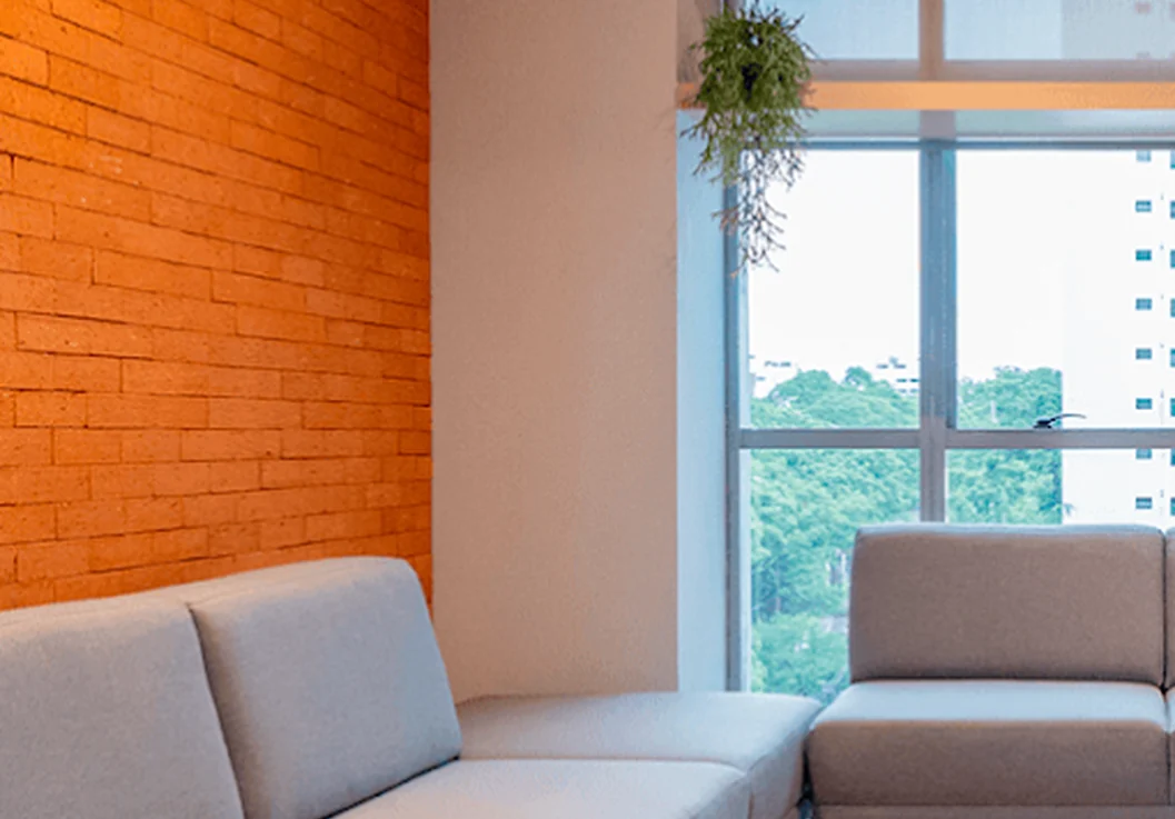 Sala com parede de tijolos laranja, sofás e janelas com vista para as árvores