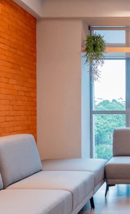 Sala com parede de tijolos laranja, sofá e janela com vista para as árvores